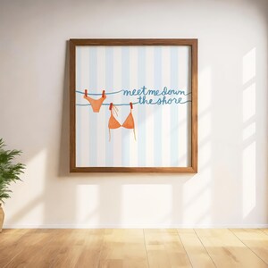 May include: A framed print featuring a watercolor illustration of a bikini top and bottom hanging on a clothesline. The background has blue and white stripes, and the text "meet me down the shore" is written in blue script.