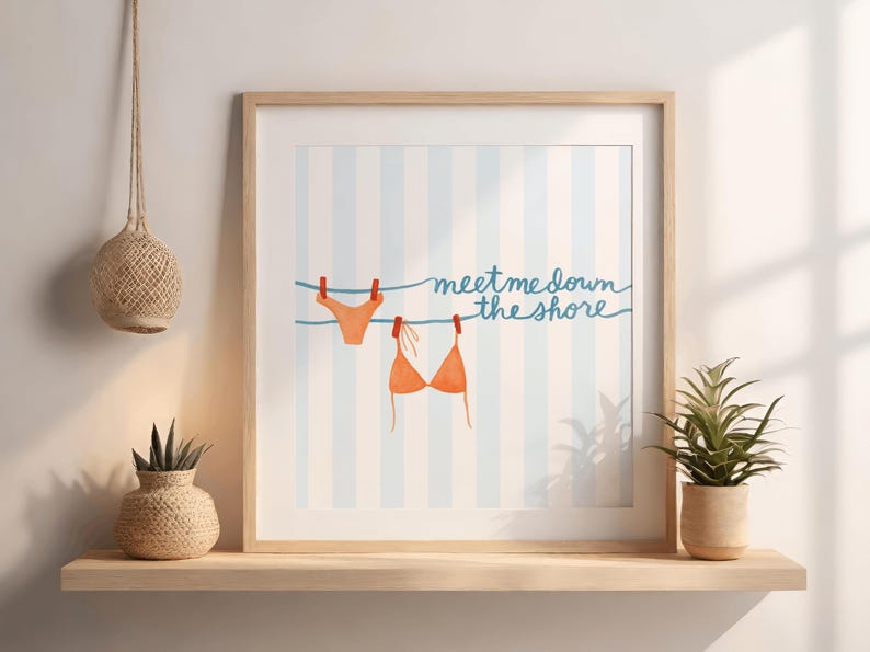 May include: Framed art print featuring an orange bikini top and bottom hanging on a clothesline with red clothespins. The background has blue and white vertical stripes, and the text reads "meet me down the shore."