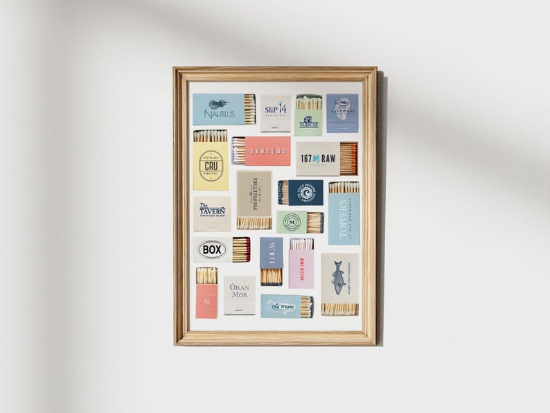 May include: A framed art print featuring a collection of matchboxes with various designs and text. The matchboxes are arranged in a grid pattern, showcasing a variety of colors and branding. The frame is a light wood color, adding a natural touch to the display.