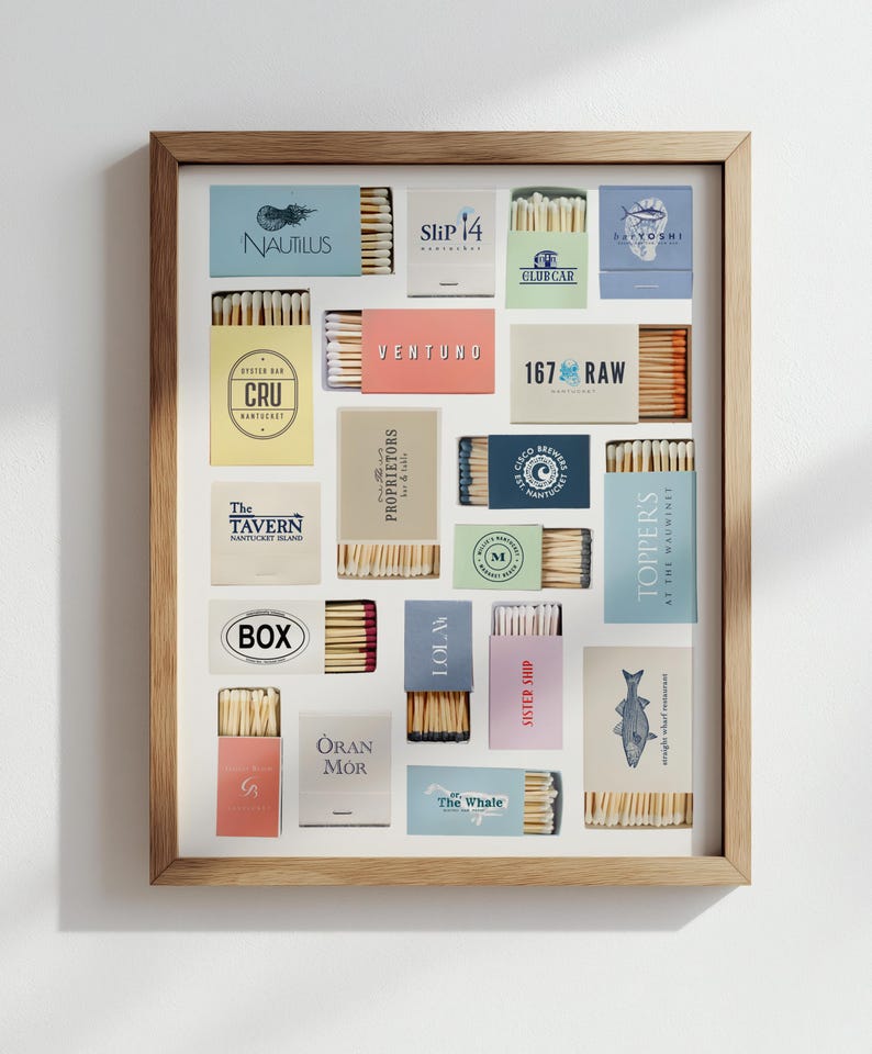 May include: A framed display featuring various matchboxes with different logos and text. The matchboxes are arranged in a grid pattern, showcasing a variety of colors and designs. The frame is made of light-colored wood.