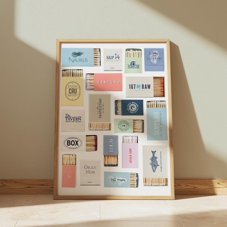 May include: A framed print featuring various matchbox designs. Each box displays a unique logo and text, including "NAUTILUS," "Slip 14," "VENTUNO," and "167 RAW." The boxes are arranged in a grid pattern, showcasing a variety of colors and styles.