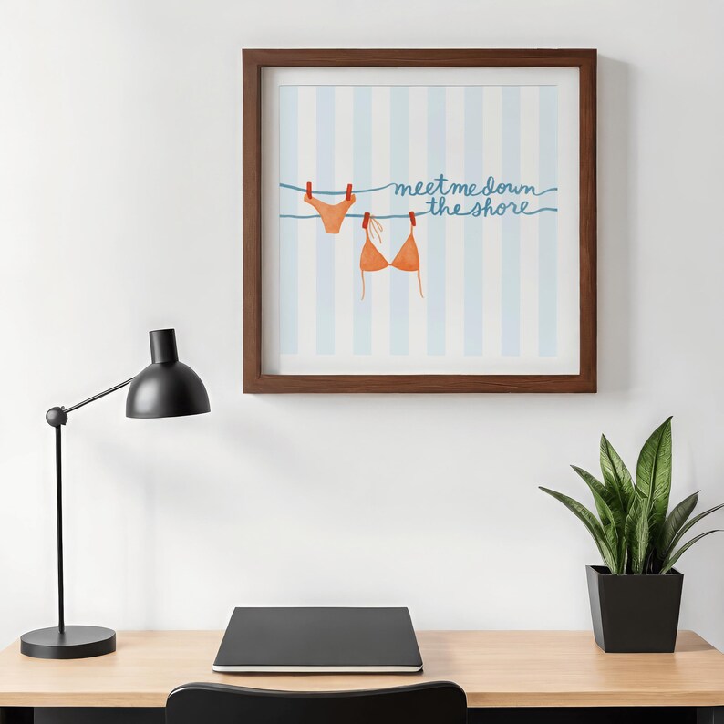 May include: A framed print featuring a watercolor illustration of a bikini top and bottom hanging on a clothesline. The background has blue and white vertical stripes, with the text "meet me down the shore" in blue script.