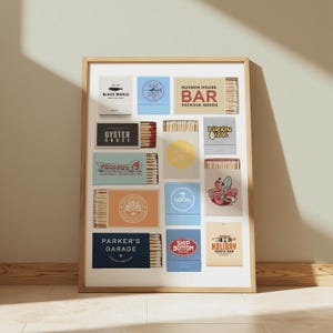 May include: A framed print featuring various matchbox designs with restaurant and bar logos. The matchboxes are in a grid pattern, showcasing diverse branding and color schemes, including "Black Whale" and "Hudson House Bar".