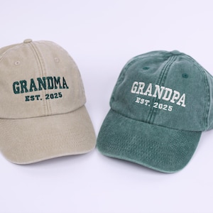 May include: Two baseball caps, one tan and one green, with embroidered text. The tan cap says "Grandma Est. 2025" and the green cap says "Grandpa Est. 2025".