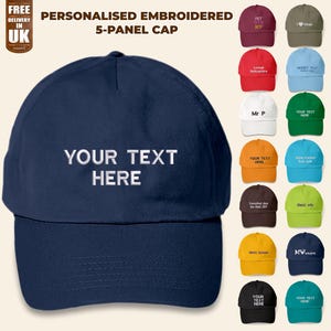 May include: A navy blue 5-panel cap with a white embroidered text that says "YOUR TEXT HERE". The cap is shown with other caps in various colors and designs.