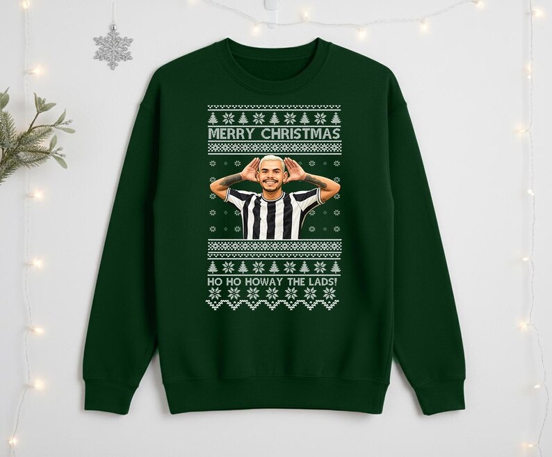 May include: A dark green Christmas sweater with a festive design. The sweater features the text "MERRY CHRISTMAS" and "HO HO HOWAY THE LADS!" in white. A person is in the center of the sweater. The sweater has a crew neck and long sleeves.