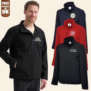 Può includere: Una giacca softshell nera, rossa e blu navy con chiusura a zip. La giacca ha un colletto alto e due tasche anteriori. La giacca è ricamata con il testo "Your Custom Text/Logo", "Custom Embroidery" e un logo.