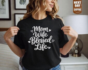 May include: Black t-shirt featuring the text "Mom Wife Blessed Life" in white script, with heart accents. The shirt is worn by a person.
