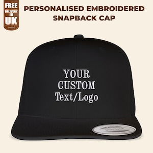 Op de afbeelding: Zwarte snapback-pet met witte borduurwerk met de tekst "YOUR CUSTOM Text/Logo".