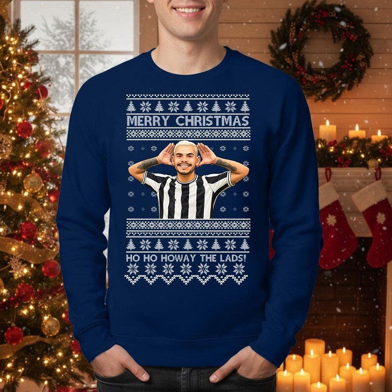 May include: Navy blue Christmas sweater with a festive design. The sweater features the text "MERRY CHRISTMAS" and "HO HO HOWAY THE LADS!" along with a graphic of a person. The design includes snowflakes and Christmas trees.