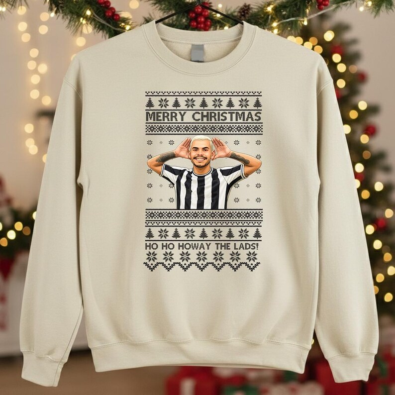 May include: Beige sweatshirt with a festive Christmas design. The design includes the text "MERRY CHRISTMAS" and "HO HO HOWAY THE LADS!" along with a graphic of a person wearing a black and white striped shirt.
