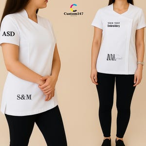 May include: Two white medical tunics with asymmetrical necklines and short sleeves are shown. One tunic has the letters "ASD" and "S&M" printed on it. The other tunic has the text "YOUR TEXT Embroidery" and a logo printed on it. Both are paired with black leggings.