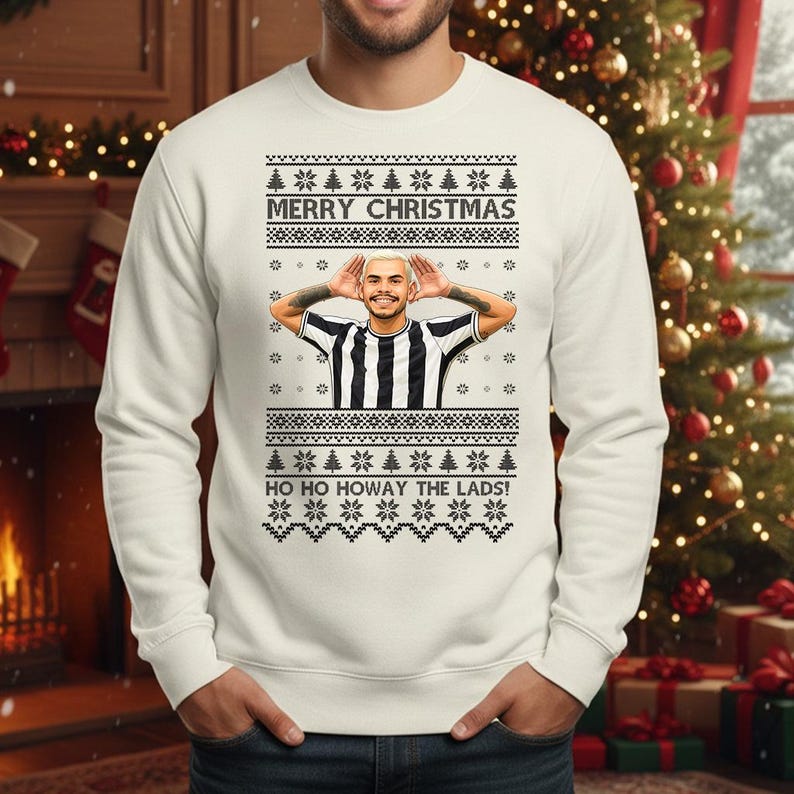 May include: A white Christmas sweater with a festive design. The sweater features the text "MERRY CHRISTMAS" and "HO HO HOWAY THE LADS!". It has a graphic of a person in a black and white striped shirt.