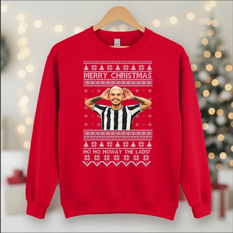 May include: A red Christmas sweatshirt with a festive design. The sweatshirt features the text "MERRY CHRISTMAS" and "HO HO HOWAY THE LADS!" in white, along with a graphic of a person wearing a black and white striped shirt. The design includes snowflakes and Christmas trees.