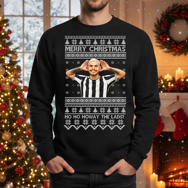 May include: Black Christmas sweater with a festive design. The sweater features the text "MERRY CHRISTMAS" and "HO HO HOWAY THE LADS!" along with a picture of a person. The sweater has a classic crew neck.