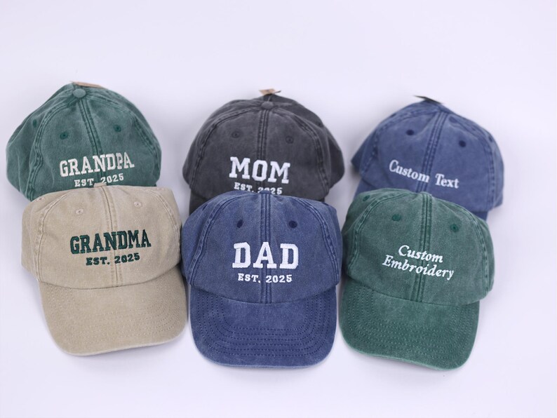 May include: Six different colored baseball caps with embroidered text. The caps are green, blue, grey, tan, and two shades of green. The text on the caps reads "Grandpa Est. 2025", "Mom Est. 2025", "Custom Text", "Grandma Est. 2025", "Dad Est. 2025", and "Custom Embroidery".