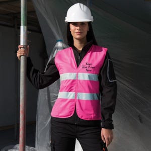May include: A pink safety vest with reflective strips and the text "Your Text/Logo Here" embroidered on the front. The vest is worn by a person wearing a white hard hat.