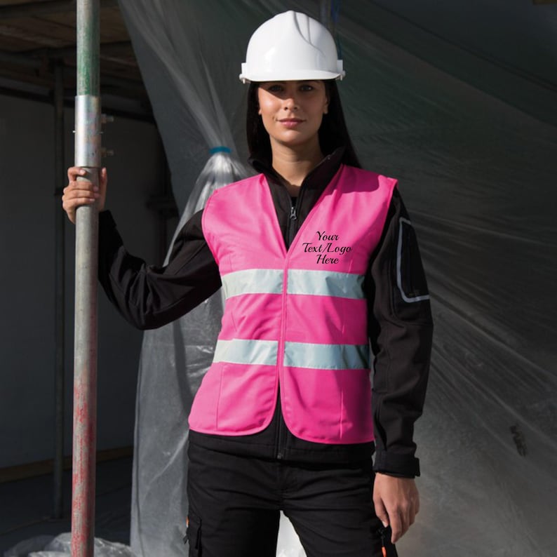 May include: A pink safety vest with reflective strips and the text "Your Text/Logo Here" embroidered on the front. The vest is worn by a person wearing a white hard hat.