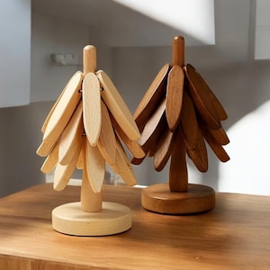 Puede incluir: Dos adornos de árbol de Navidad de madera, uno en madera natural y otro en madera marrón. Los adornos están hechos de piezas que se entrelazan y se asemejan a ramas de árbol.