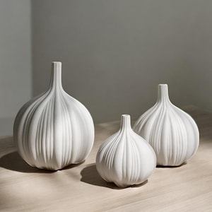 May include: Three white ceramic vases shaped like garlic bulbs. The vases are arranged in a row, from largest to smallest.