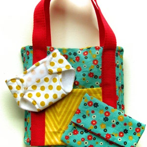Könnte beinhalten: Eine rote und weiße Tragetasche mit einem gelben und weißen Chevron-Muster und einem Blumendruck. Die Tasche hat zwei rote Henkel und eine kleine weiße und gelbe Windel im Inneren. Es gibt auch eine kleine türkisfarbene Clutch mit Blumendruck.