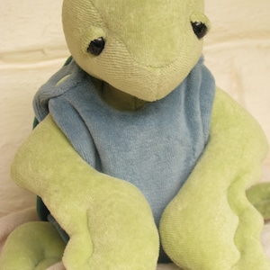 May include: A plush green turtle toy with a blue fabric shell. The turtle has black eyes and a soft, cuddly texture.