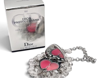 May include: A Dior Pretty Charms 002 Pink Enchantment lip gloss compact in a silver box. The heart-shaped silver pendant features a pink lip gloss interior and is surrounded by clear crystal beads on a silver chain, with 1.5 g - 0.05 oz net weight.