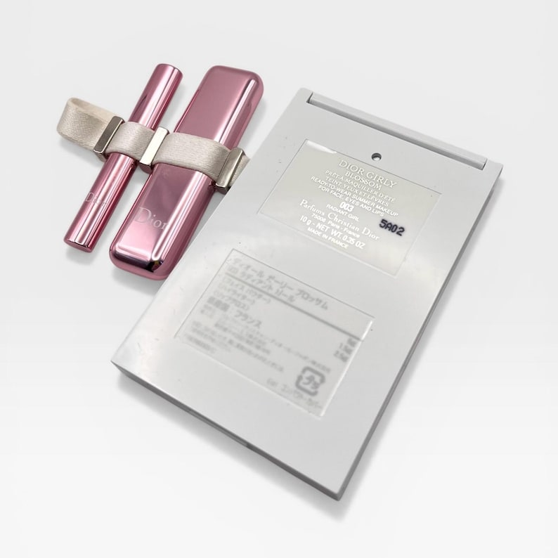 May include: A pink Dior makeup set featuring a lipstick, a lip gloss, and a compact. The lipstick and lip gloss are held together with a beige ribbon. The compact is rectangular and has text on it.