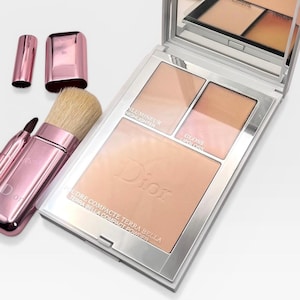 May include: A Dior Terra Bella compact powder palette with a mirror, highlighter, bronzer, and lip gloss. Includes a pink makeup brush and a pink lipstick tube. The palette is in a silver case.