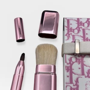 May include: A set of pink makeup brushes and a compact. The brushes include a large powder brush, a small angled brush, and a liner brush. The compact is white with a pink pattern and a white strap.