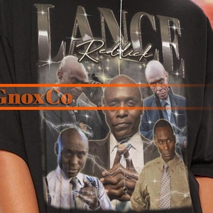 May include: Black t-shirt with a graphic print of four men's faces. The text "Lance Reddick" and "GnoxCo" are printed on the shirt.