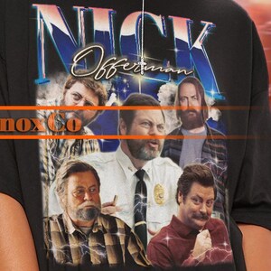 May include: Black unisex t-shirt with a vintage graphic of Nick Offerman and other actors. The shirt features the name "NICK" in a stylized font. The text "Gnox Co" is also visible. The model wears a 2XL sized shirt.