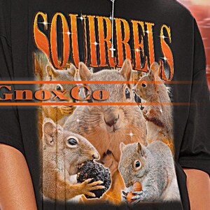 Könnte beinhalten: Schwarzes Unisex-T-Shirt mit einem Eichhörnchen-Motiv und dem Wort "SQUIRRELS" in Orange. Das Shirt hat auch den Text "Gno&Co" in Orange. Das Shirt ist von TSHIRT Unisex.