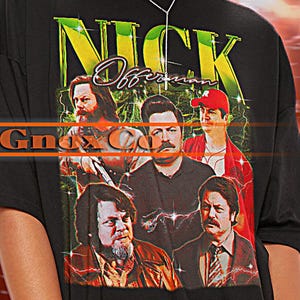 May include: Black t-shirt featuring a graphic print of a band called "Nick Offerman & The Gnarly Companions". The shirt is oversized and has a distressed look.