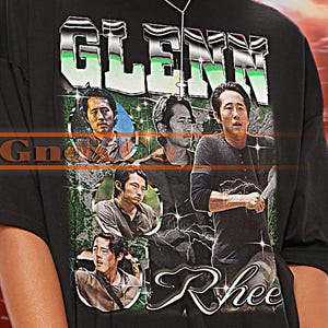 Puede incluir: Camiseta negra de gran tamaño con el nombre "GLENN" en verde y plata, e imágenes de una persona. La camiseta también incluye el nombre "Rhee". El texto "TSHIRT Unisex" está en la parte superior.