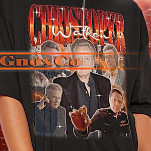 Könnte beinhalten: Schwarzes Unisex-T-Shirt mit dem Namen "Christopher Walken" im Vintage-Stil. Das Shirt zeigt eine Grafik von Christopher Walken und den Text "Gmax Co". Das Model trägt Größe 2XL.