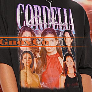 May include: Black oversized t-shirt with a graphic print of a group of women and the text "CORDELIA" in a purple and pink font. The text "Ginaxxx Co" is printed in a white font below the graphic.