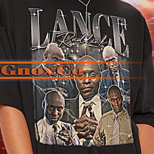 May include: Black unisex t-shirt featuring a graphic of several men with the text "LANCE Rebirth" and "Ginox". The shirt has short sleeves and a crew neck. The brand name "TSHIRT Unisex" is at the top left.