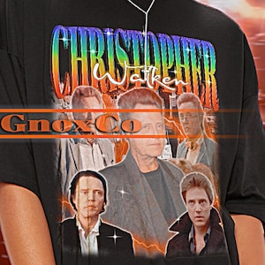 Könnte beinhalten: Schwarzes Unisex-T-Shirt mit einem farbenfrohen Christopher Walken-Motiv und dem Text "CHRISTOPHER Walken". Das Shirt hat kurze Ärmel und einen Rundhalsausschnitt. Der Markenname "TSHIRT Unisex" steht oben links.