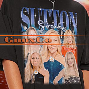 Puede incluir: Camiseta unisex negra con un gráfico de mujeres y el texto "Sutton Stracke". La camiseta también tiene el texto "Tshirt Unisex" y "Gnox Co". La modelo lleva la camiseta.