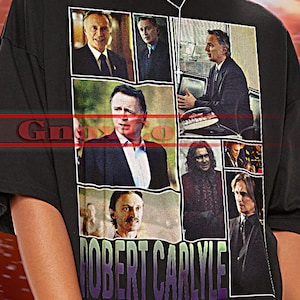 May include: Black unisex t-shirt featuring a collage of images and the name "ROBERT CARLYLE". The shirt has the text "TSHIRT Unisex" at the top. The model is wearing the shirt. The shirt is true to size.
