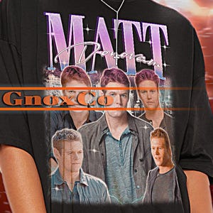 May include: Black oversized t-shirt featuring a vintage-style graphic of a band called "Matt Doran". The graphic shows a group of five men with the band's name in a pink and purple font.