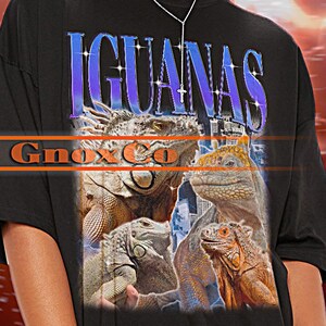 Könnte beinhalten: Schwarzes Unisex-T-Shirt mit dem Wort "IGUANAS" in einem lila-blauen Farbverlauf. Das Shirt hat eine Grafik von mehreren Leguanen. Der Markenname "Ginox & Co" ist ebenfalls sichtbar. Das Shirt ist übergroß.