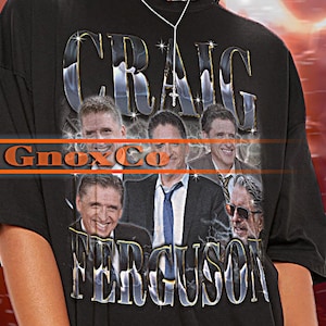 May include: Black unisex t-shirt with a graphic print of a group of men with the text "Craig Ferguson" and "GnoxCo" on the front. The model is wearing a 2XL sized shirt.