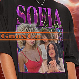 May include: Black unisex t-shirt featuring the text "SOFIA" in purple and green, with a photo of three women. The shirt also has the text "Gnox Co" and "Tshirt Unisex". The model is wearing the 2XL sized shirt.