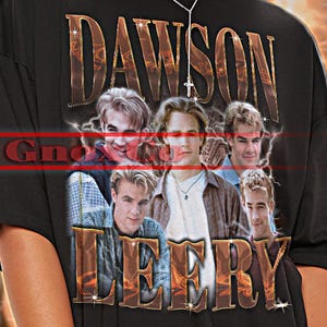 May include: Black unisex t-shirt featuring the text "DAWSON LEERY" above a photo of a group of young men. The shirt also has the text "TSHIRT Unisex" at the top. The shirt is a unisex style.
