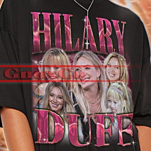 Könnte beinhalten: Schwarzes Unisex-T-Shirt mit dem pinkfarbenen Schriftzug "HILARY DUFF" und Bildern von Hilary Duff. Das Shirt hat auch den Text "TSHIRT Unisex" oben. Das T-Shirt ist ein Unisex-Stil.