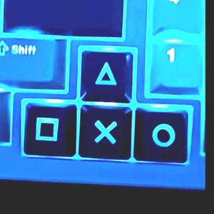 May include: Close-up of a blue game controller with illuminated buttons. The image shows the 'Shift' key, a square, an 'X', a triangle, and a circle button. The number '1' is also visible.