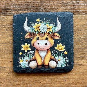 Peut inclure: Un dessous de verre carré en ardoise noire avec un dessin de taureau de dessin animé. Le taureau est brun clair avec des cornes blanches et un nez rose, portant une couronne florale.