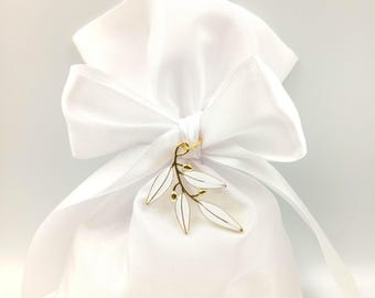 May include: A white satin gift bag tied with a matching bow. A gold-toned leaf charm with white enamel leaves adorns the bow. The bag is filled and ready for gifting.